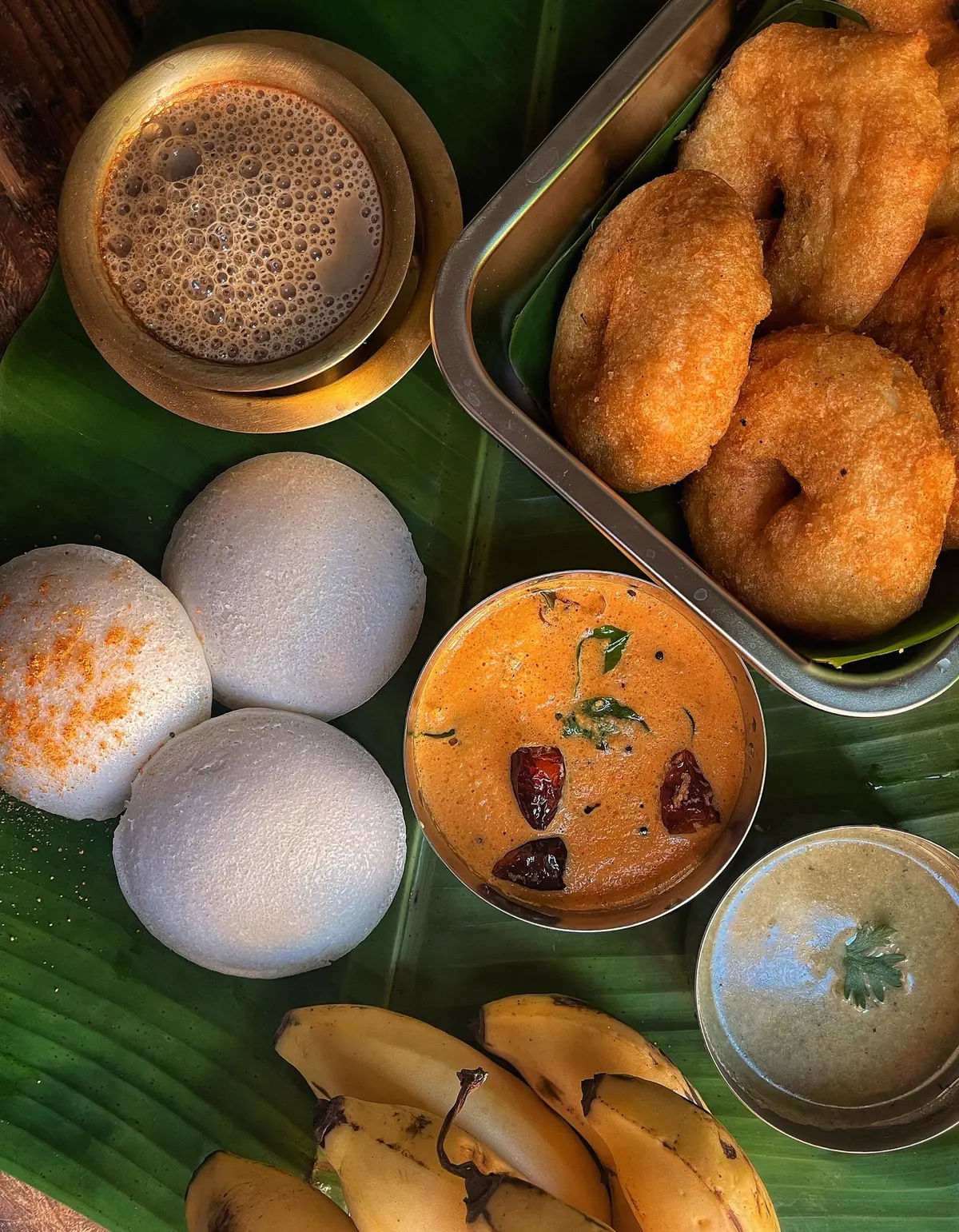 Idli, medu vada, sambar, chutneys and filter coffee on a banana leaf