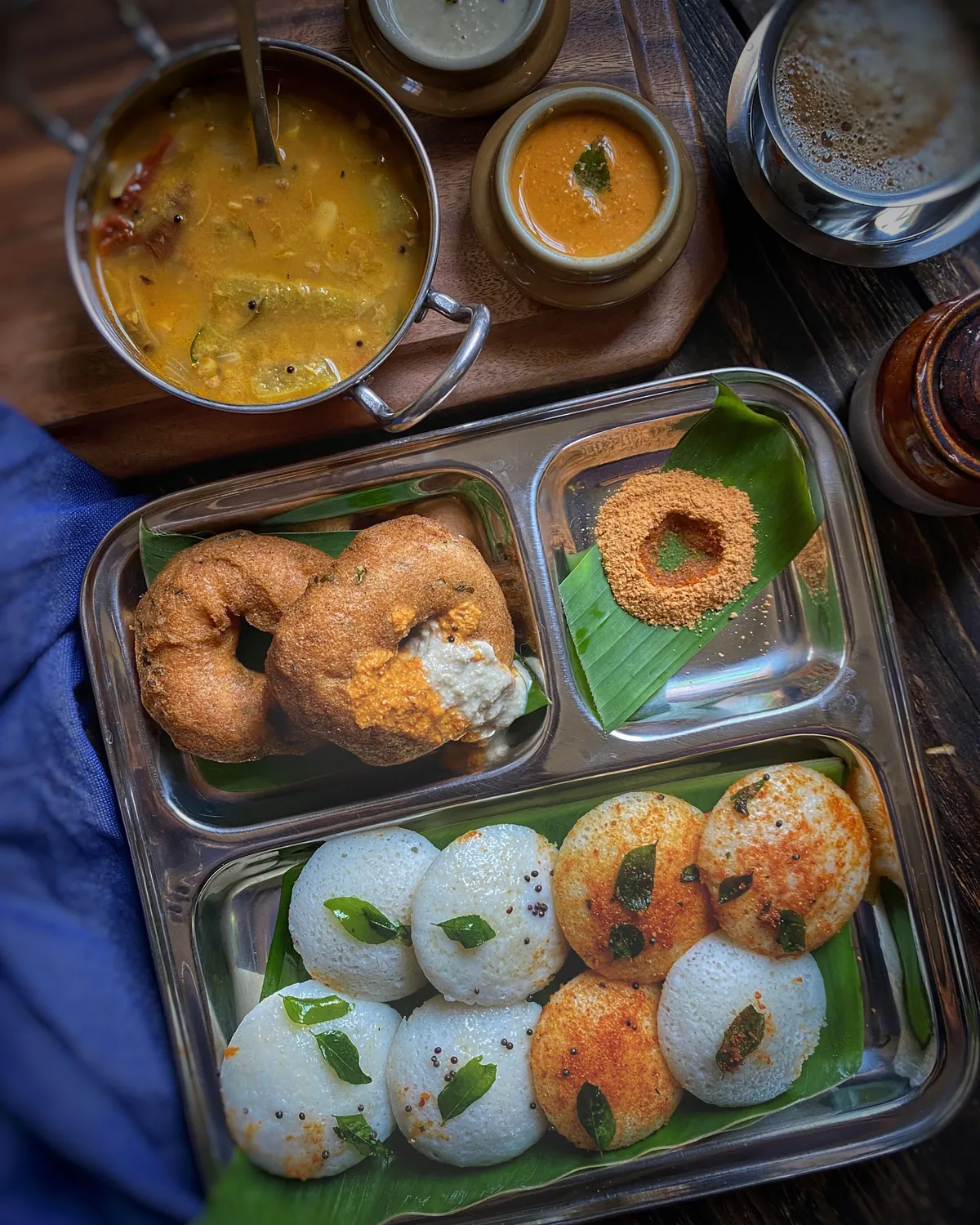 Idli, medu vada, sambar, chutneys and filter coffee on a steel plate